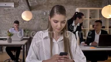 年轻漂亮的女商人正在办公室里用智能手机<strong>打字</strong>，她的同事正在与科技建立<strong>联系</strong>